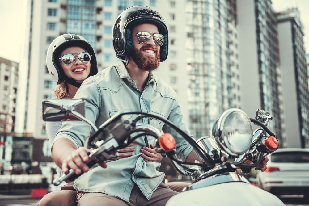 Beautiful young couple in Solid-Tinted sunglasses and helmets is smiling while riding a motorcycle